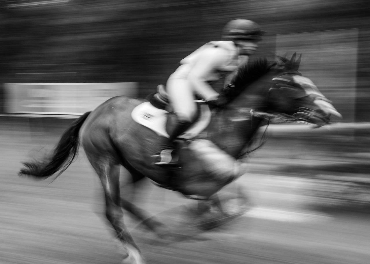Black and white motion blur of a jockey crouched over a galloping racehorse