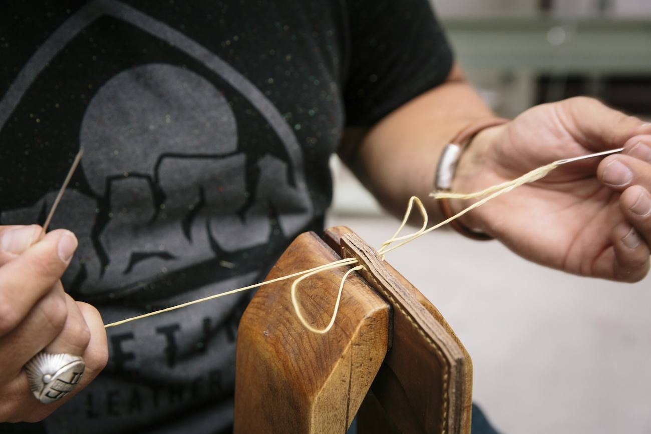 A leatherworker hand-stitching leather held in a wooden stitching clamp